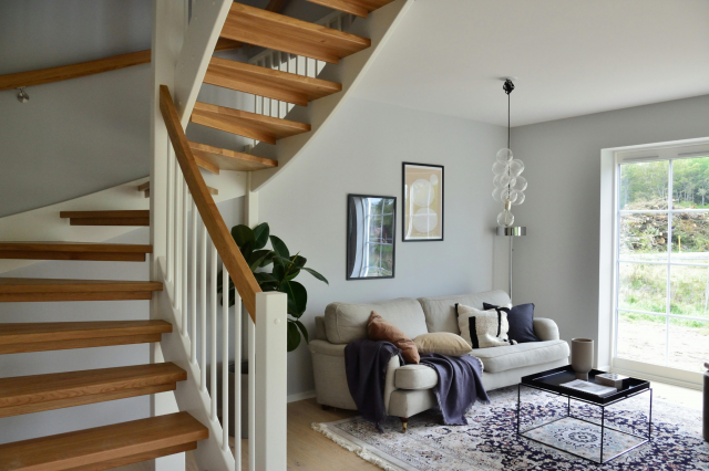 ahşap merdiven basamakları ve beyaz ferforje korkuluklarıyla boyanmış dubleks ev merdivenin evin beyaz duvarı ve açık renk mobilyalarıyla yakaladığı ferah havayı açıklayan görsel